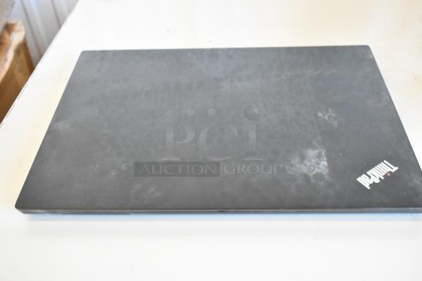 Closed Lenovo ThinkPad laptop on white surface, showing a worn black top with ThinkPad logo in the corner.