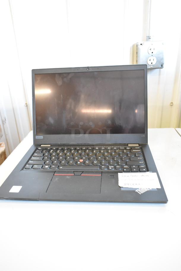 Lenovo ThinkPad L13 laptop, black, with visible keyboard wear, on white surface. Paper note showing product details.