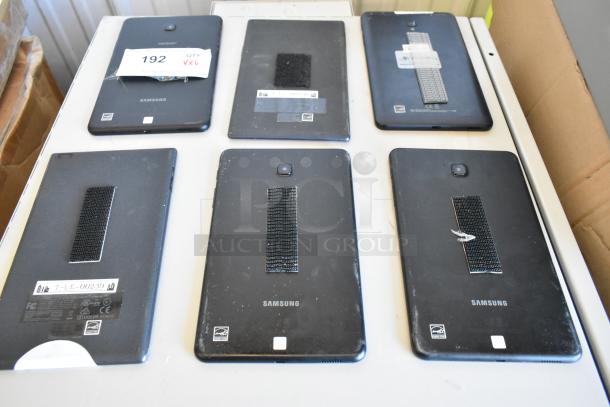 Six assorted tablets including Samsung models, visible wear, Velcro strips on back, various labels, auction lot 192.