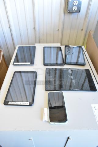 Six assorted tablets on a table, various brands and sizes. Some have visible wear, including one with a cracked screen.