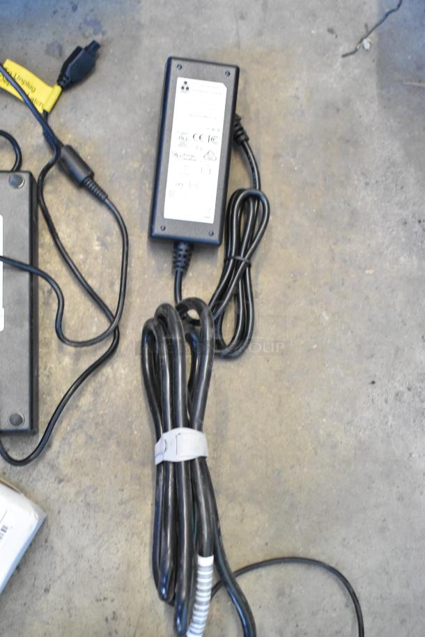 Lot of miscellaneous items including a power adapter with visible label, coiled black wires, and a yellow-tagged cord.