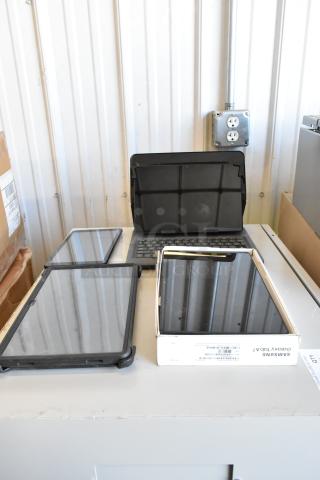 Four various tablets, including a Samsung Galaxy Tab A7, on a table. Good condition, some with cases. Includes packaging.