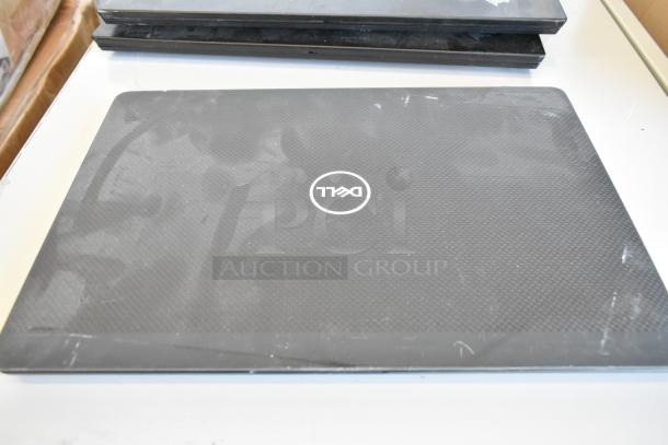 Five assorted laptops, including Dell and HP, some surface wear visible, stacked on a table.
