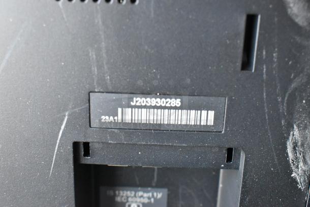 Close-up of back panel on Elo monitor showing barcode and serial number J203930285. Scratches visible on black surface.