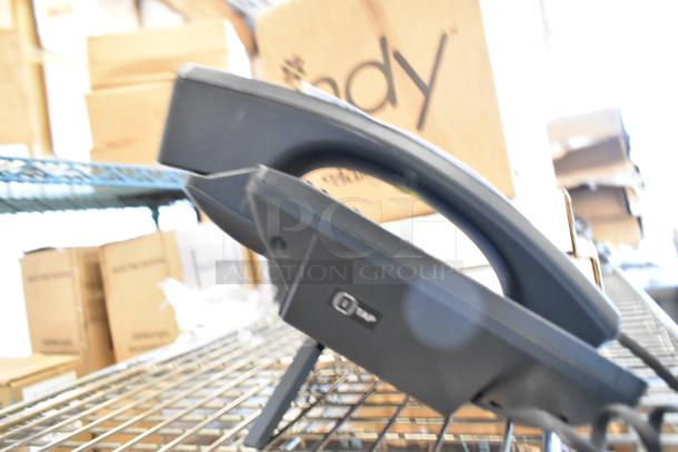Verizon corded office telephone with a black handset, resting on a metal shelf in a warehouse. Boxes visible in the background.