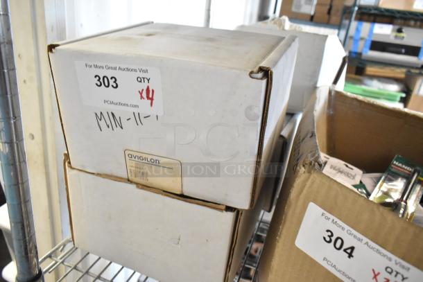 Four brand new Avigilon cameras in original boxes, labeled with model and auction details, on a metal shelf.