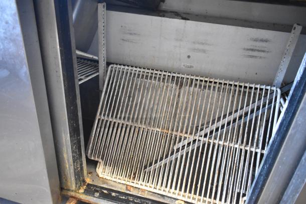 Inside view of a True TSSU-72-30M-S stainless steel commercial prep table, showing two white wire shelves and signs of wear.