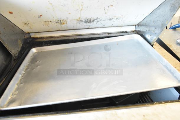 Aluminum tray inside a commercial kitchen prep table, showing wear and food residue.