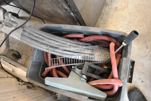 Poly bin containing assorted items, including red hoses, metal rod, and a gray tool handle. Mixed condition.