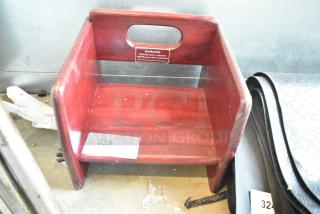 Wooden booster seat, reddish finish, with handle cutout. Visible "WARNING" label for child safety. Auction label "325."