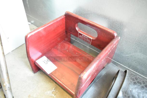 Red wooden booster seat with a cutout handle, minor wear, and a visible warning label; auction tag number 325.