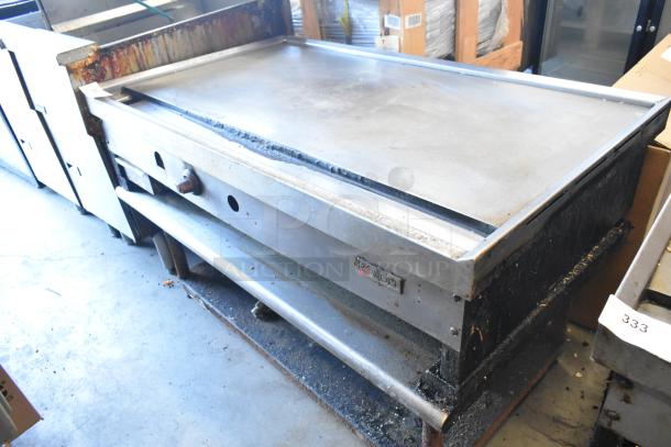 Wolf stainless steel commercial gas griddle on metal stand, used condition, with metal under shelf and visible Wolf branding.