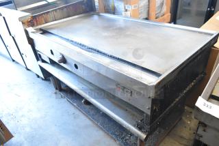 Wolf stainless steel commercial gas griddle on metal stand, used condition, with metal under shelf and visible Wolf branding.