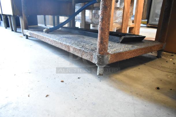 Wolf stainless steel commercial gas griddle with rusted metal stand and shelf, showing signs of wear, piping visible.
