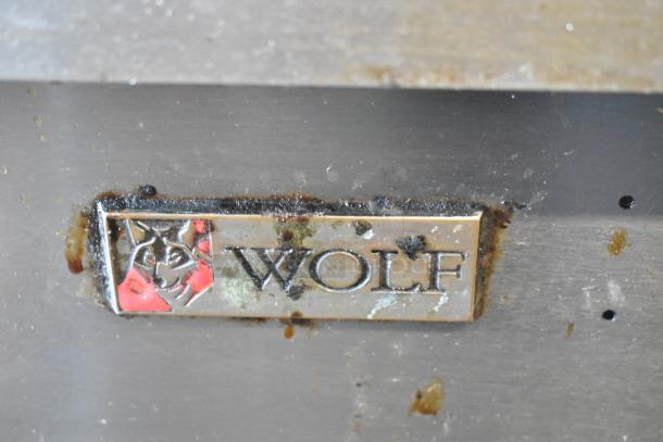 Wolf stainless steel commercial gas griddle on metal stand with under shelf, fair condition, branded logo visible.