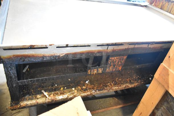 Wolf stainless steel commercial gas griddle on metal stand with under shelf; visible wear, rust, and residue present.