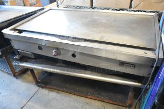 Wolf stainless steel commercial gas countertop griddle on metal stand with undershelf. Shows wear. Wolf logo visible.