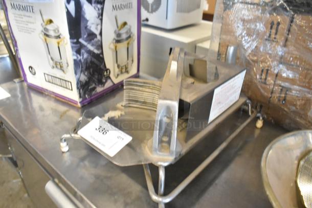 Metal countertop tomato slicer with stainless steel blades, used condition, on a kitchen counter. Auction tag visible.