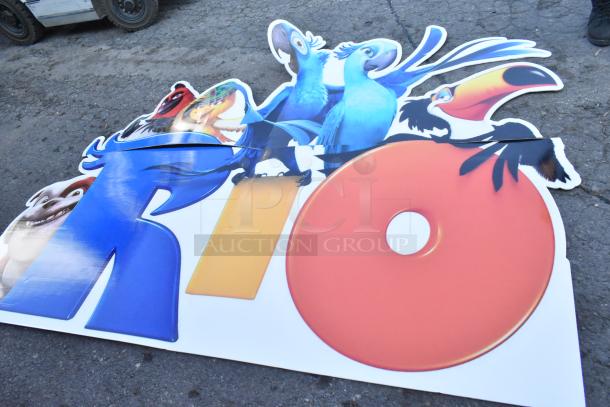 Colorful "Rio" sign featuring animated bird characters, in excellent condition, laid on pavement.