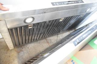 Stainless steel range hood with baffle filters, built-in lights, and digital controls, showing signs of use.