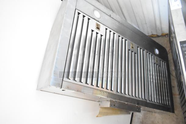Stainless steel range hood, vented, with grill-style filters, used condition, surface wear visible.