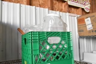 Brand new lot of items in a green crate, featuring a poly container, wrapped in plastic, with visible product labels.