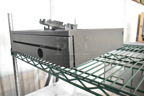 Metal cash drawer with sleek design, slot for bills, sturdy construction, and visible mounting brackets. In good condition.