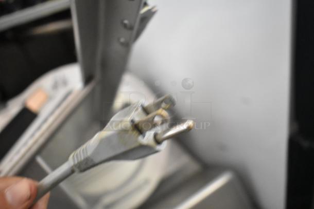 Blurry close-up of a power plug from a 2020 Bizerba GSP HD stainless steel commercial meat slicer, 120V, 1 phase.