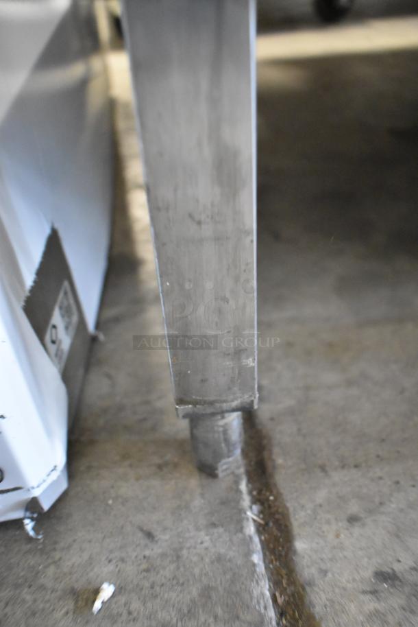 Metal table corner with under shelf, showing sturdy leg on concrete floor, highlighting industrial use.