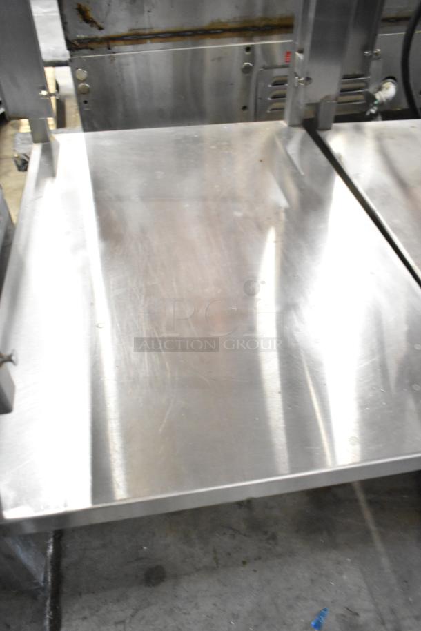 Metal table with under shelf, features a smooth surface and visible wear. Ideal for industrial or kitchen use.