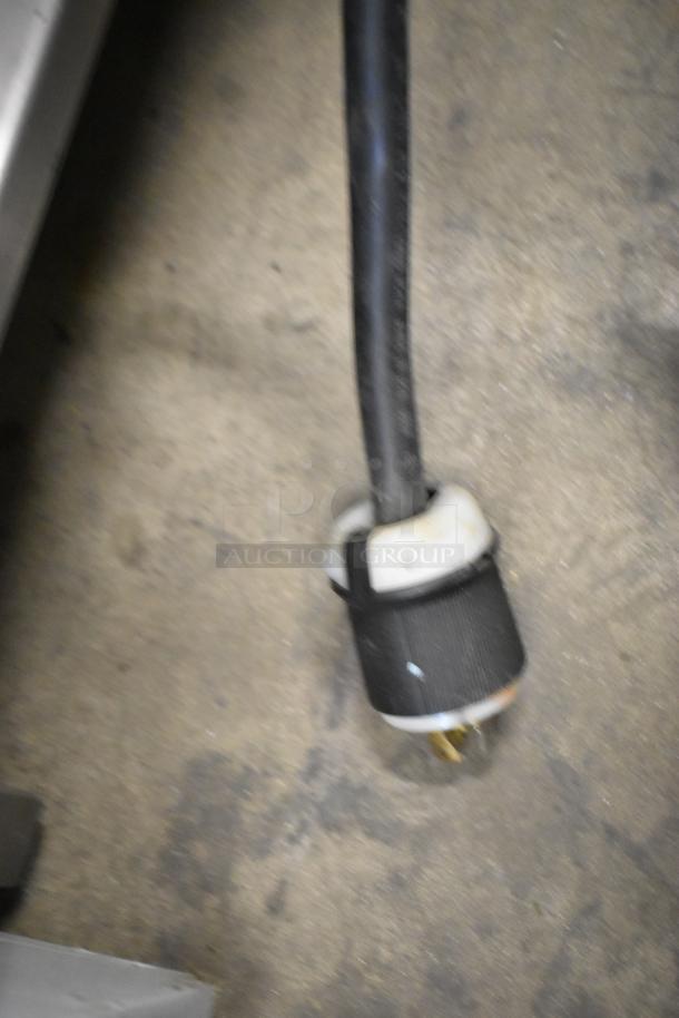 Blurry image of an electrical plug for the Cleveland 21CET8 SteamCraft Ultra 3 steam cabinet, showing wear on the flooring.
