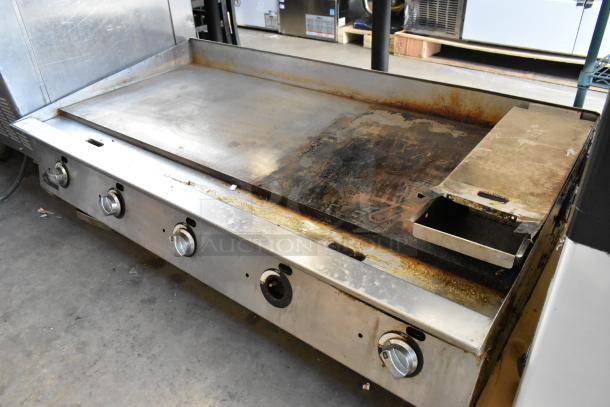 Stainless steel commercial countertop gas griddle, featuring four control knobs and flat cooking surface. Visible wear and rust.