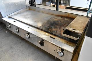 Stainless steel commercial countertop gas griddle, featuring four control knobs and flat cooking surface. Visible wear and rust.