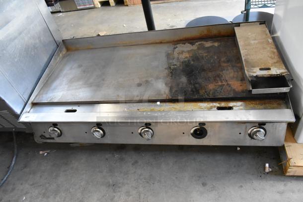 Stainless steel commercial countertop gas griddle with four control knobs, showing signs of use and surface discoloration.
