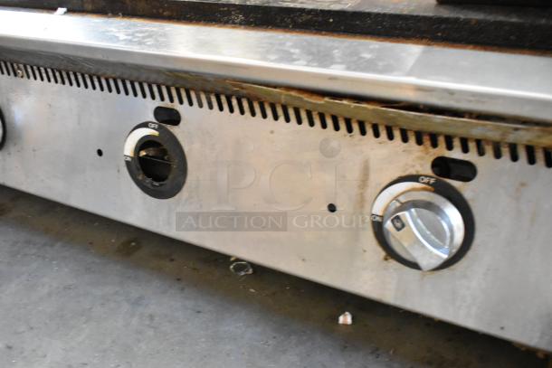 Stainless steel commercial countertop gas griddle, flat top, with control knobs. Shows signs of use, ideal for kitchens.