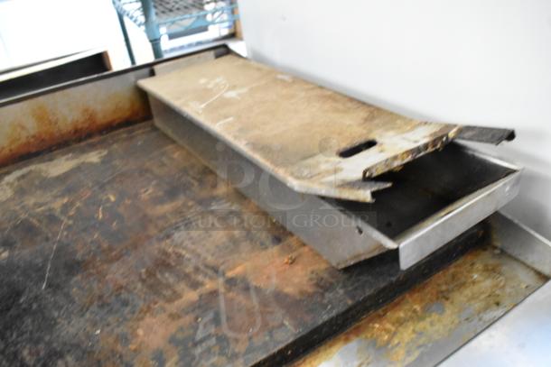 Stainless steel commercial countertop gas griddle with flat top, showing signs of wear and discoloration.