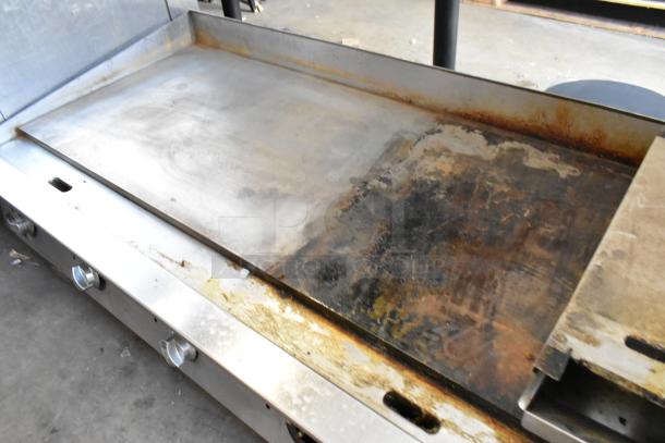 Stainless steel commercial countertop gas-powered griddle, visible wear and rust, three control knobs, flat top surface.