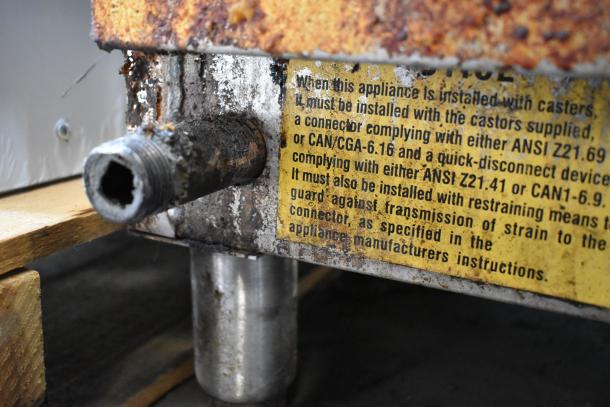 Stainless steel commercial griddle, gas-powered, showing rust and wear. Installation instructions label visible.