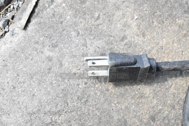 Close-up of a black two-prong electrical plug on a concrete surface.