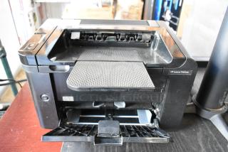 HP LaserJet P1606dn countertop printer, black, with paper tray open; visible label indicates model. Good condition.