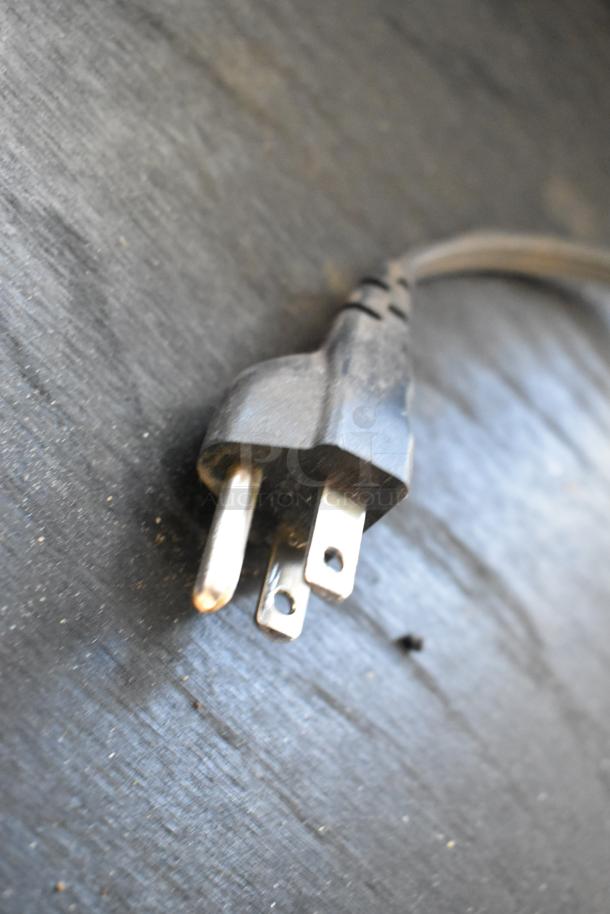Power plug for HP LaserJet P1606dn countertop printer, showing three-prong connector on dark background.