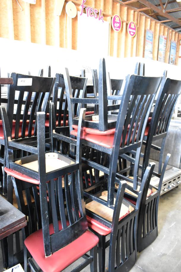 14 black dining chairs with red seat cushions, stacked in a warehouse. Solid construction, moderate wear visible.