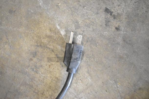 A power cord with a standard three-prong plug on a concrete floor.