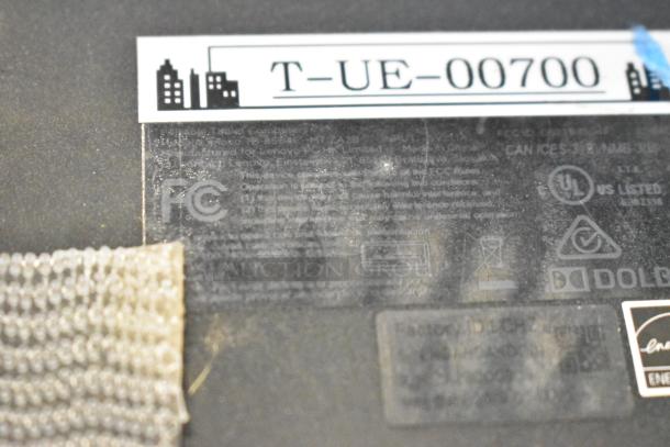 Close-up of electronic device with visible certification logos and a tag reading "T-UE-00700." Dust present, indicating used condition.