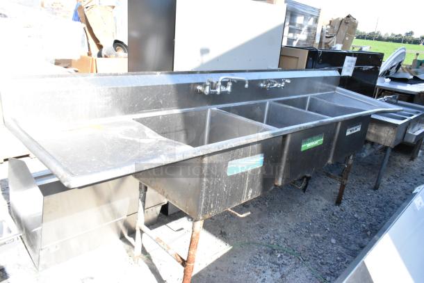 Stainless steel 3 bay sink with dual drain boards; signs of wear visible. Ideal for commercial kitchen use.