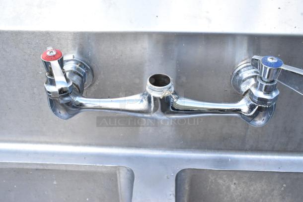 Alt text: Stainless steel 3-bay sink with dual drainboards, featuring hot and cold water handles and a central faucet mount.