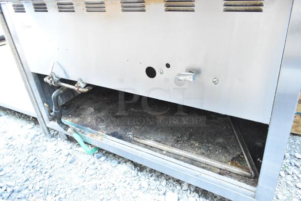 Stainless steel commercial steam table with visible gas connections. Signs of use and wear on the surface.