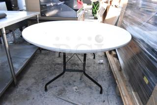 White round folding table with black metal legs, outdoor setting. Good condition, ideal for events, easily portable.