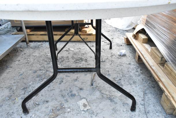 White round folding table with black metal legs, sturdy design, suitable for indoor or outdoor use. Slightly worn condition.