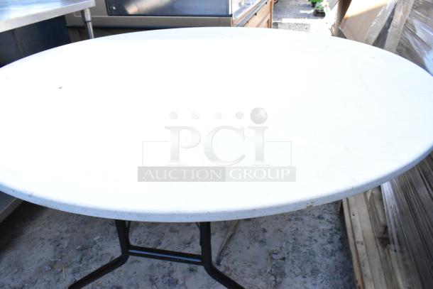 White round folding table with a durable surface and sturdy metal legs, suitable for indoor or outdoor use. Slight wear visible.